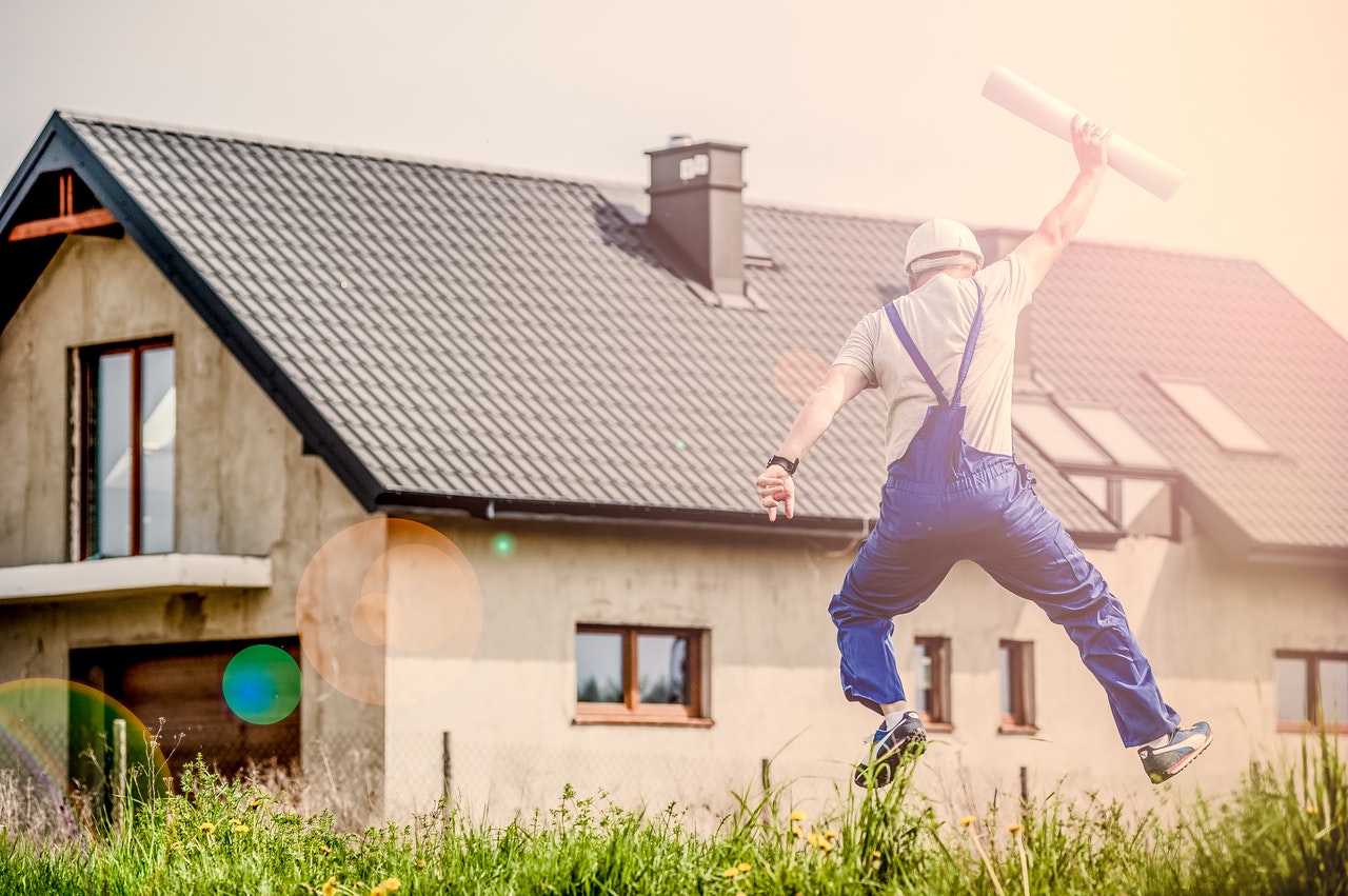 Builder jumping for joy holding plans in front of a house in summer